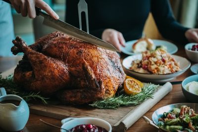une dinde en train d’être découpée sur un comptoir avec de la sauce aux canneberges, des légumes et de la purée de pommes de terre