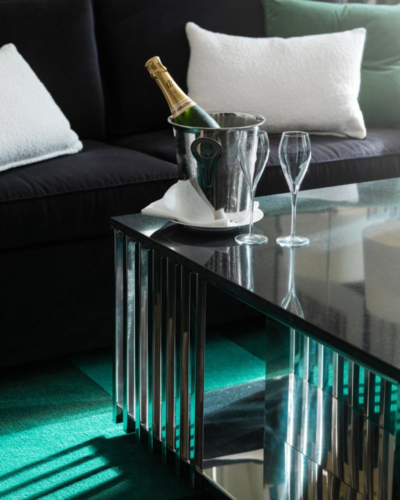 A chilled bottle of champagne in a silver bucket with two crystal flutes on a modern glass table within a Sofitel London St James Prestige Suite.