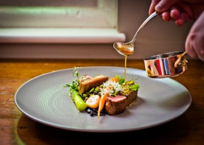 A jus being poured over an elegantly plated main at a fine dining restaurant