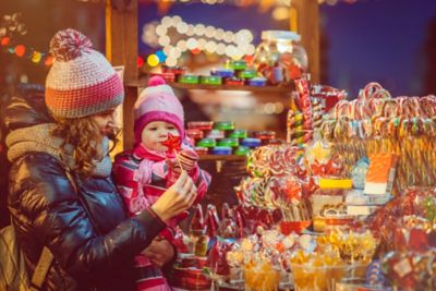 Une mère et sa fille dans les bras, devant un stand de sucreries dans un marché de Noël