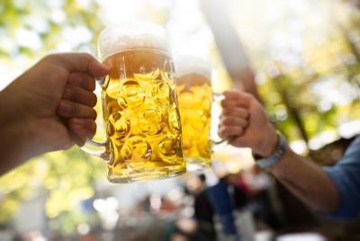 Zwei gefüllte gläserne Bierkrüge, mit denen in einem Münchner Biergarten angestoßen wird