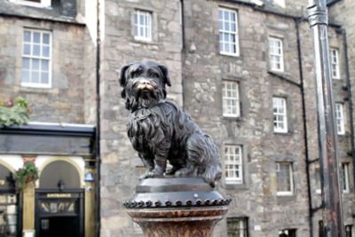 Estatua de bronce de Greyfriars Bobby en Edimburgo, Escocia, frente a un edificio de piedra