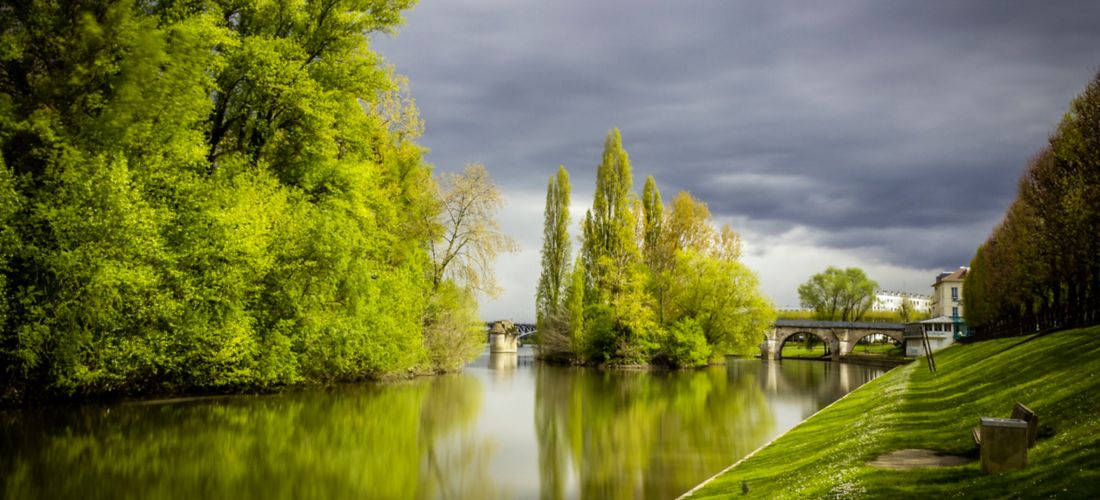 Serene Water Canal with Trees and Approaching Storm Clouds