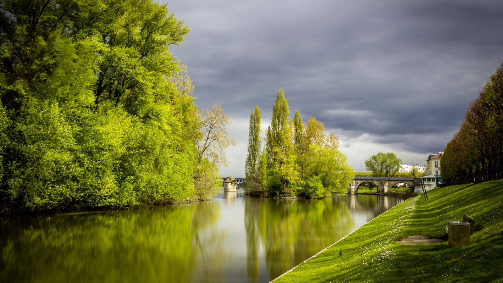 Serene Water Canal with Trees and Approaching Storm Clouds
