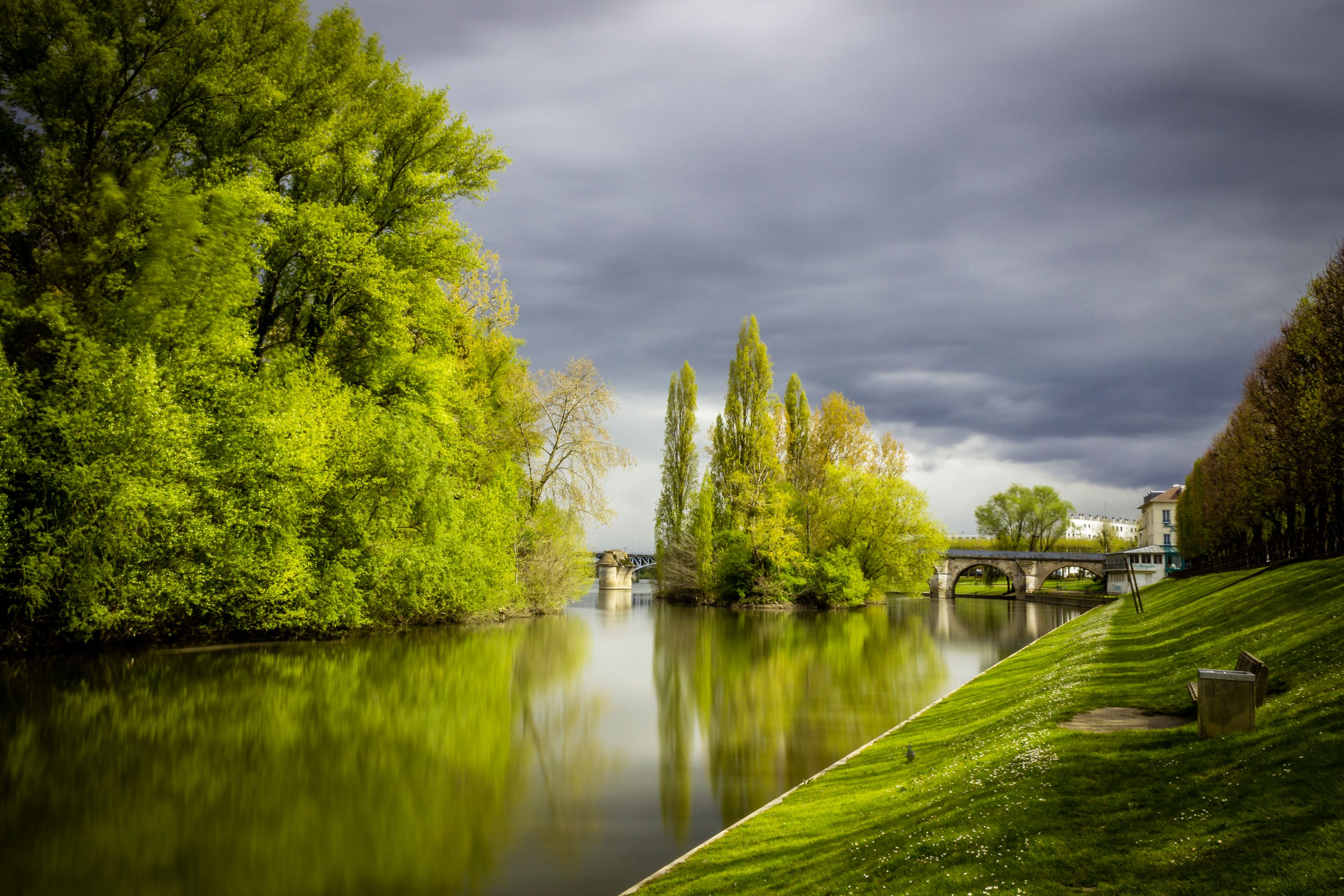 Serene Water Canal with Trees and Approaching Storm Clouds