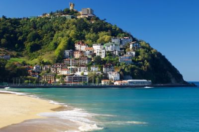 Playa de Ondarreta, colina verde con edificios y un castillo bajo un cielo azul claro