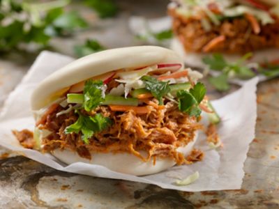A pulled pork bao bun garnished with fresh coriander and vegetables