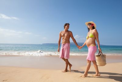 An expectant couple on a babymoon strolling hand-in-hand down a quiet beach