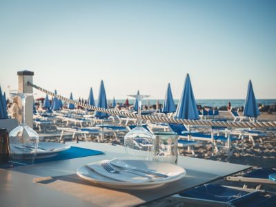 A table set for dinner overlooking a sandy beach and blue sea at sunset