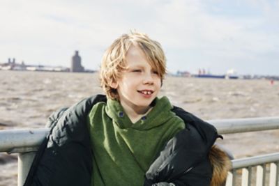 Smiling child with tousled blond hair in front of the River Mersey with skyline silhouette