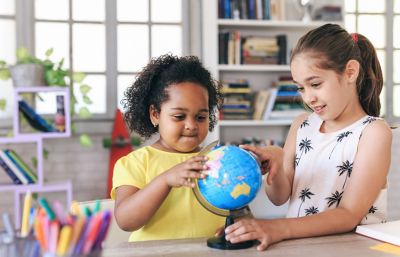 Dos niñas sonríen mientras miran y tocan un globo terráqueo azul en una habitación luminosa