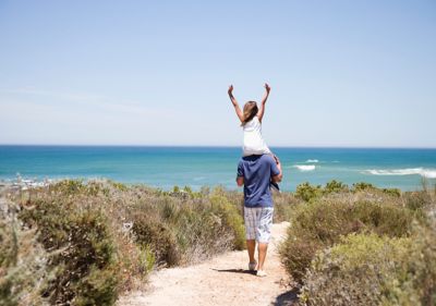 A child on the shoulders of their parent, gazing at the sea