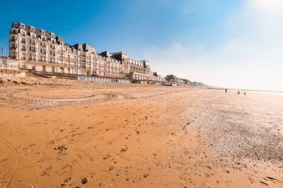 Grande plage de sable à Cabourg, bordée de maisons de style Belle Époque, avec des promeneurs