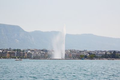 Die Wasserfontäne des Jet d'Eau im Genfersee mit Hausfassaden am Ufer im Hintergrund