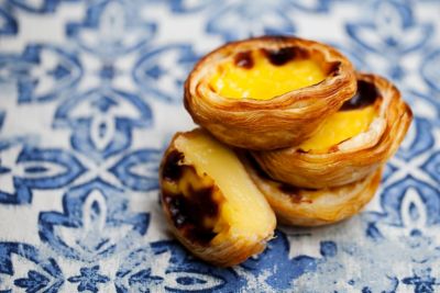 Drei Pastéis de Nata, ein bekanntes portugiesisches Gebäck, auf blauen Azulejo-Fliesen