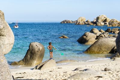 A young child with a fishing net on a rocky beach during a family holiday in France