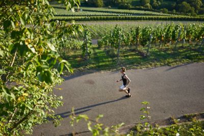 A runner on a wide, flat road in a vineyard on a sunny day