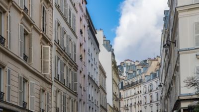 Calle estrecha con fachadas clásicas de balcones y contraventanas blancas bajo un cielo nublado