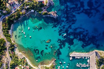 Curved bay in Corfu in the Ionian Sea with a marina, blue waters, leafy trees and a coastal road