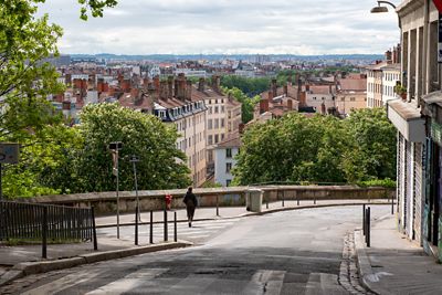 Calle empinada de Lyon con techos rojos, chimeneas y una persona caminando hacia el horizonte