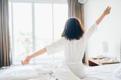A traveller stretching as the morning sun streams into their hotel room