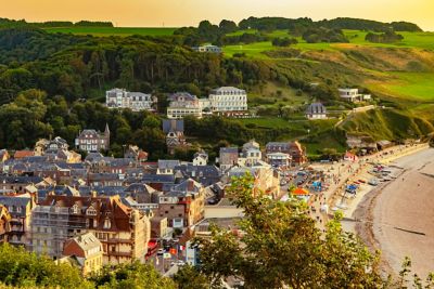Village d’Étretat sur la côte normande, avec les toits des maisons colorés par l’heure dorée de fin de journée et les vacanciers qui se baladent sur la promenade en bord de mer