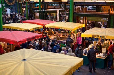 Shoppers browsing stalls covered with red and yellow umbrellas at Borough Market in London