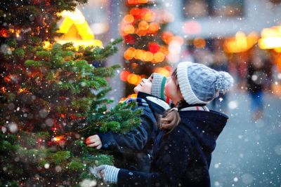 two children standing in a snowy alley looking at a christmas tree