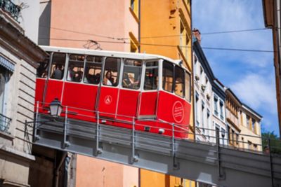 Funicular rojo ascendiendo por una estructura metálica en Lyon, bajo un cielo azul despejado