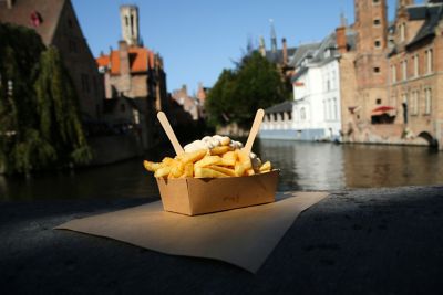 Ein Pappschälchen mit belgischen Fritten vor einem Kanal mit historischen Häusern in Brügge