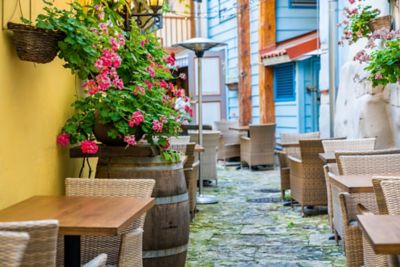 Historischer Innenhof in der Altstadt von Tallinn mit Korbstühlen an Holztischen und bunten Blumen