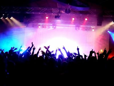 A colourfully lit stage at a rock concert with the silhouette of spectators