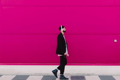 Un jeune homme écoute de la musique en passant devant un mur rose