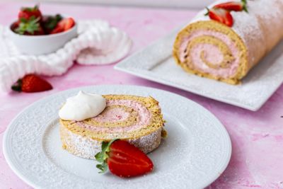 Biskuitroulade mit Topfen-Erdbeercreme, garniert mit Sahne und Erdbeeren