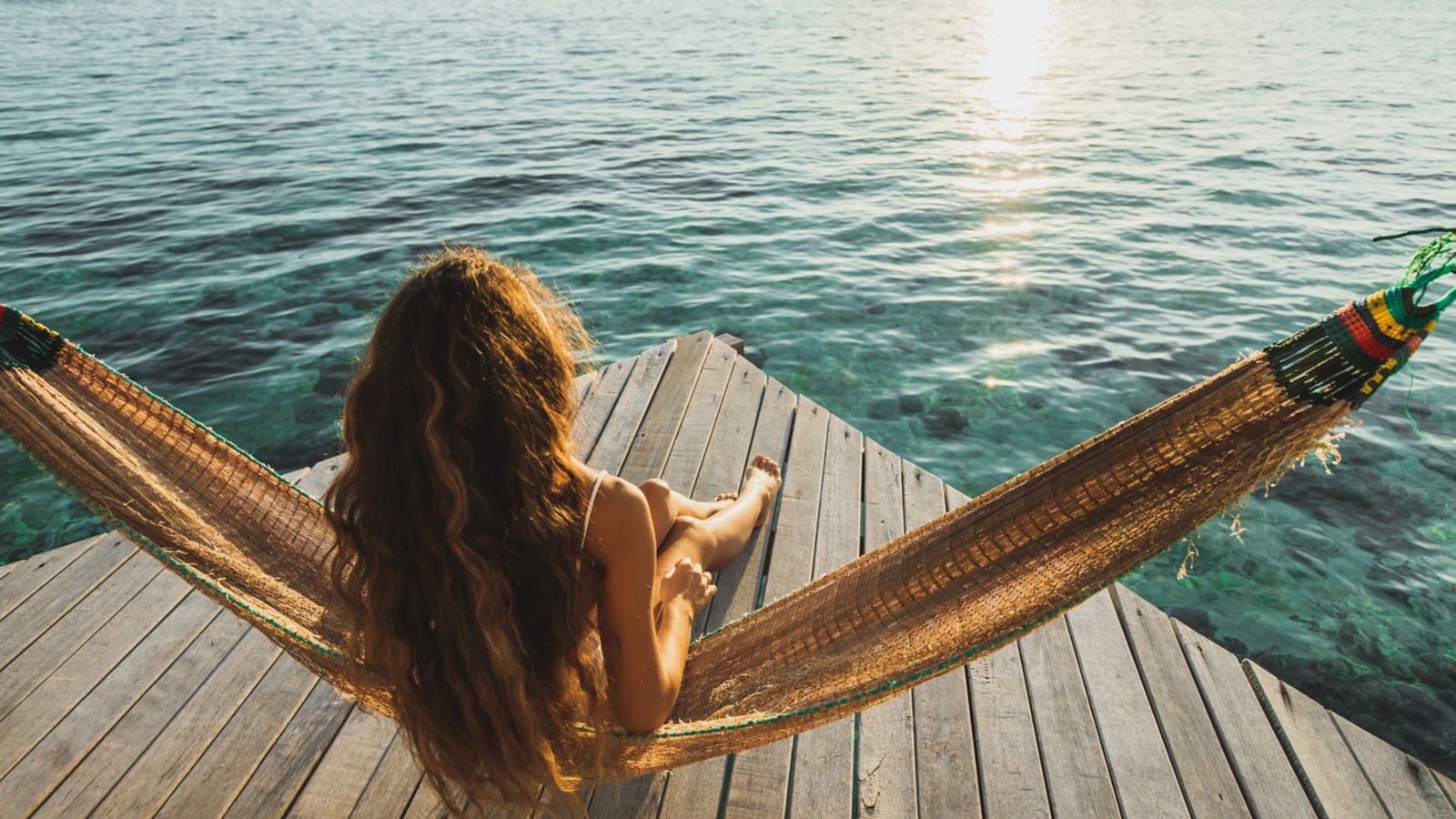 Femme installée sur un hamac face au coucher de soleil lors de vacances reposantes