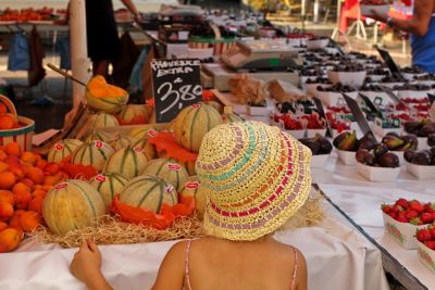 A straw-hatted child looking at fruit on display at a market in Provence, France
