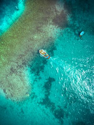 Ein einzelnes kleines Boot treibt im türkisblauen Wasser des Gardasees, aus der Luft gesehen