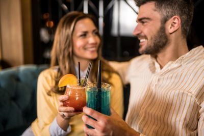 Smiling couple toasting with colourful cocktails in a sophisticated lounge bar