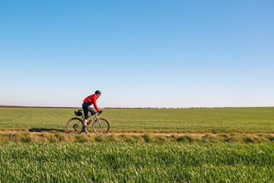 A cyclist passing through open fields against a cloudless blue sky in England