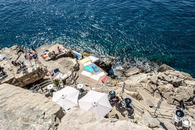 Sunbathers, towels and umbrellas on the rock platforms of Buža Beach overlooking the Adriatic Sea