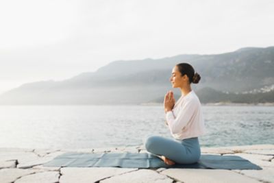 A person sitting in a prayer pose on a yoga mat by a tranquil sea