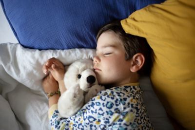 A young child asleep on a comfortable bed, cuddling a white teddy