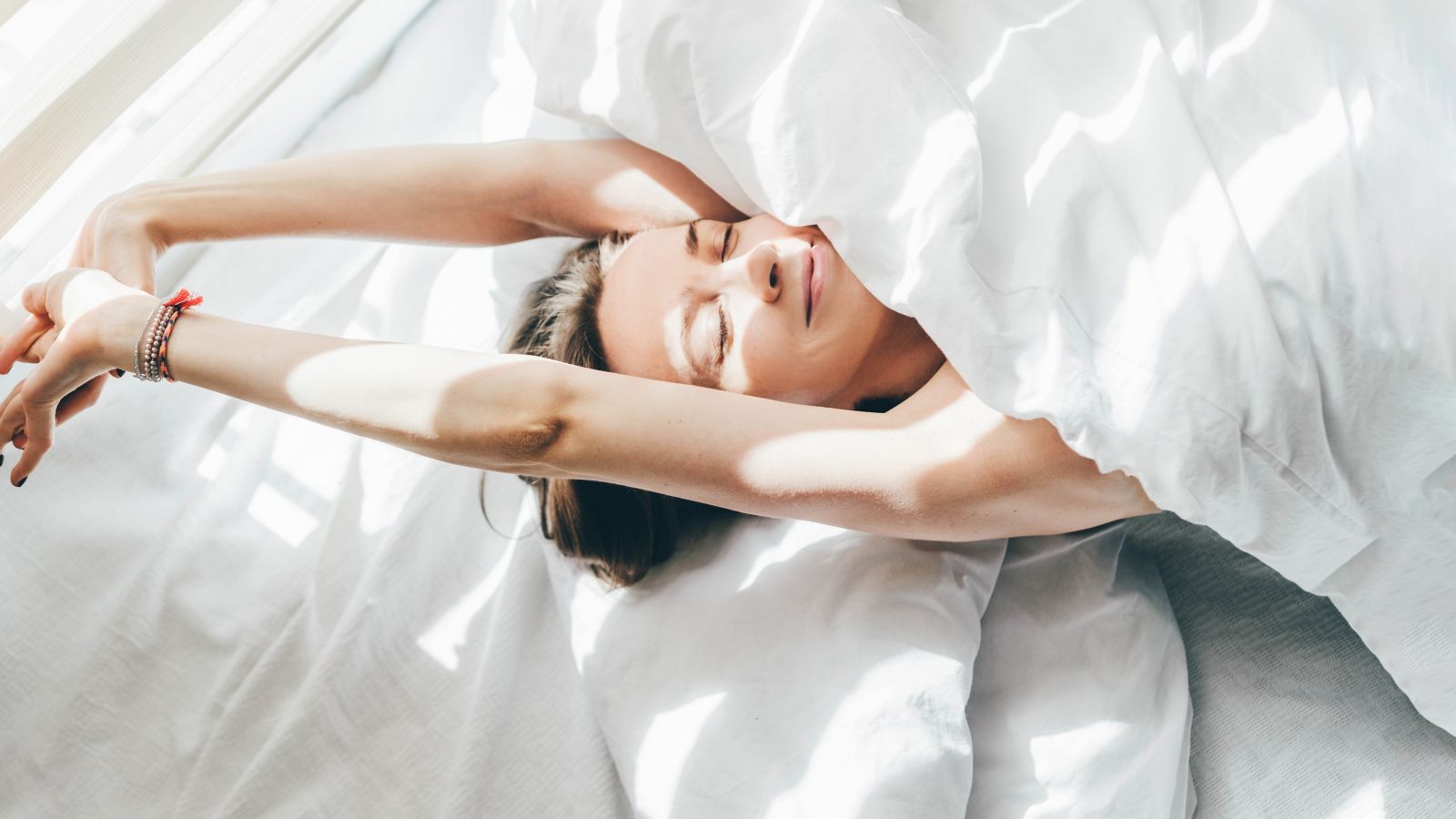 A smiling person stretching blissfully under a fluffy white duvet