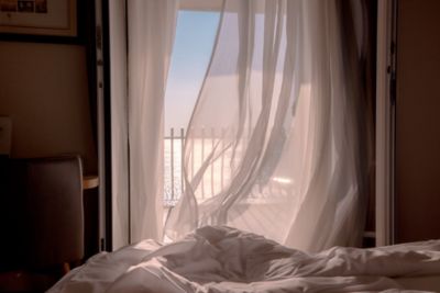 A sea view through gauzy white bedroom curtains blowing in the breeze