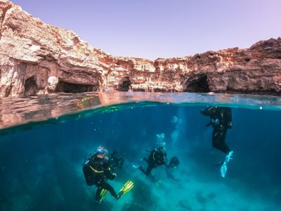 Scuba divers exploring the blue waters of a shallow, rocky cove in Malta