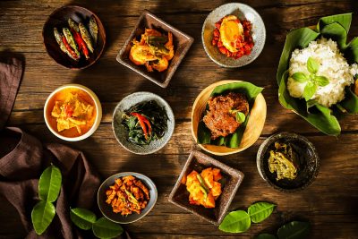 Nasi Padang, a rice meal from Padang, Minang, West Sumatra. The rice is accompanied with various side dishes to choose from. Here each side dish is plated individually. The dishes are arranged on a rustic wooden table. A crumpled linen napkin is placed on the lower left corner. Some kaffir lime leaves are placed on the table.