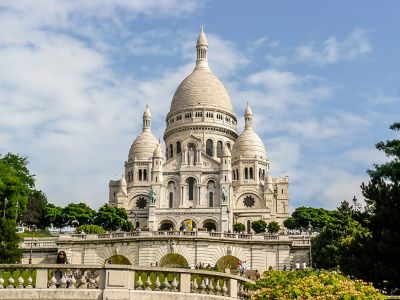 Basílica del Sagrado Corazón en París bajo un cielo azul con nubes ligeras y jardines verdes