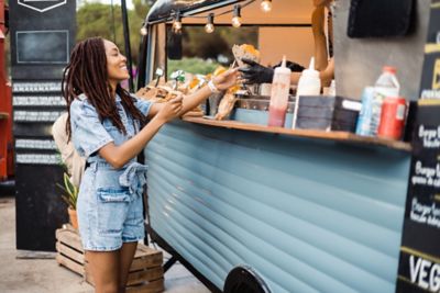 Foodtruck, an dem eine lächelnde junge Frau Fastfood in einer Papiertüte kauft