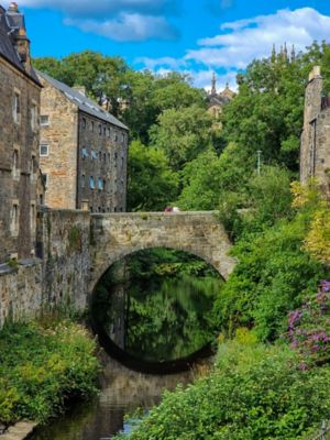 Pueblo medieval con puente de piedra sobre un río rodeado de vegetación y edificios antiguos
