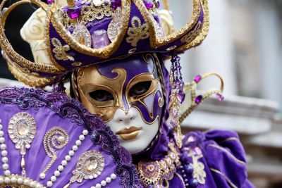 Une personne costumée en violet et doré, portant un masque, au carnaval de Venise